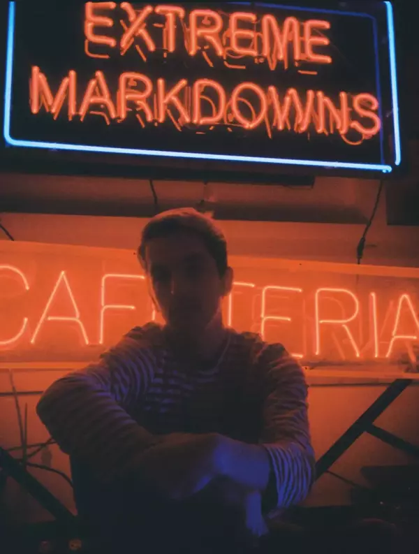 Aaron Campbell, wearing a red striped shirt, sitting in front of neon signs, animated stereoscopic wigglegram image